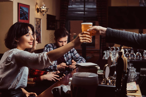 Νέοι φίλοι πολυφυλετικής σε bar. μπάρμαν δίνοντας ποτήρι μπύρα στον πελάτη σε παμπ. - Φωτογραφία, εικόνα