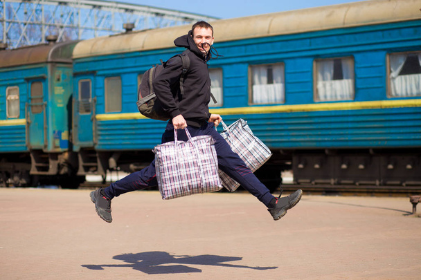 Молодий чоловік з великими сумками біжить на залізничній станції. Подорож поїздом
 - Фото, зображення