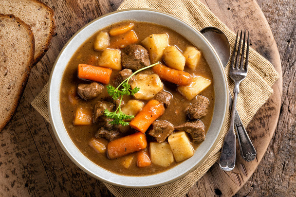 Een kom heerlijke zelfgemaakte rundvlees stoofpot met wortelen, aardappelen, ajuin en raap. - Foto, afbeelding