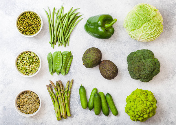 Assorted green toned raw organic vegetables on white background. Avocado, cabbage, broccoli, cauliflower and cucumber with trimmed and mung beans, pak choi, loose pepper and lettuce - 写真・画像