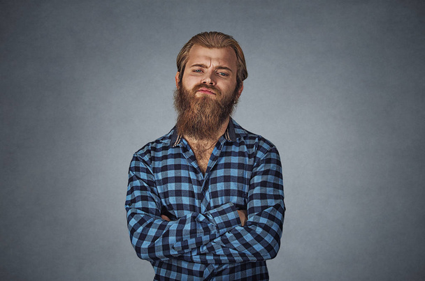 Portrait of angry discontent young bearded man with bristle wears shirt looks unhappy and keeps hands crossed. Hipster man with beard in blue plaid checkered shirt  Isolated on gray studio Background - Photo, Image