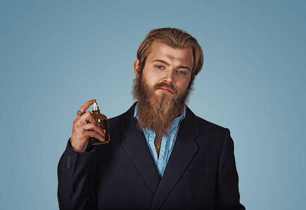 Rich man expensive using perfume eau de cologne, eau de toilette. Bearded hipster businessman Isolated on blue Background. Horizontal Studio shot. - Fotó, kép