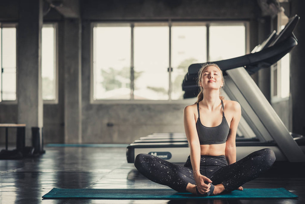 Счастливая белая женщина, растянувшаяся на коврике для йоги перед тренировкой в спортзале
 - Фото, изображение