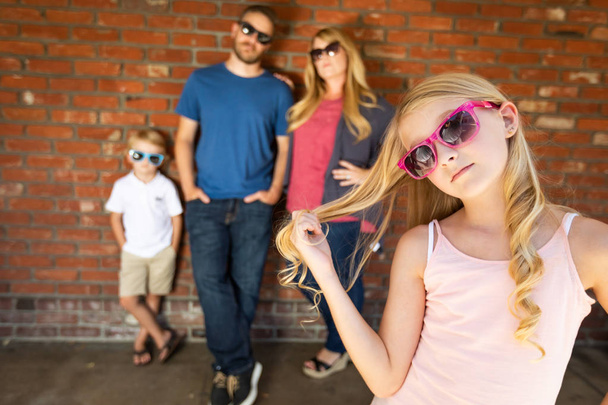 Linda joven caucásica chica usando gafas de sol con familia detrás
. - Foto, Imagen