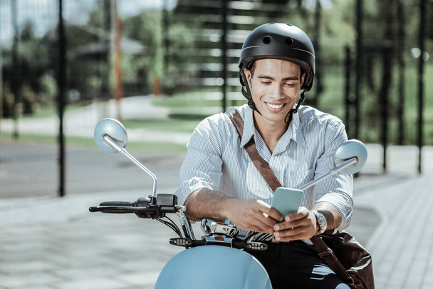 Cheerful jovial guy reading message on motorbike - Photo, Image