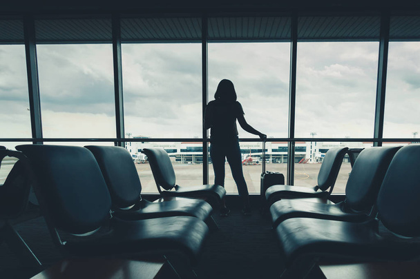 Silhouette tourist woman is talking on mobile phone while standing in passengers airport terminal. - 写真・画像