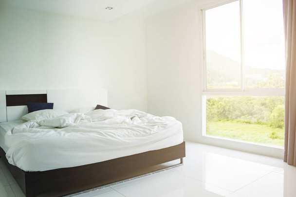 Oreiller blanc, couverture blanche et serviette blanche sur le lit dans la chambre avec un éclairage doux le matin
. - Photo, image