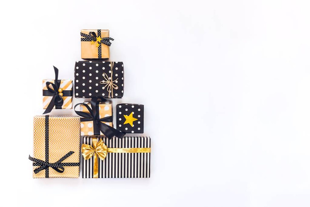 Ansicht von Geschenkboxen in verschiedenen schwarzen, weißen und goldenen Designs, die in dreieckiger Form wie Weihnachtsbaum oder Geburtstagstorte angeordnet sind. ein Konzept von Weihnachten, Neujahr, Geburtstagsfeier. flache Lage, Kopierraum. - Foto, Bild