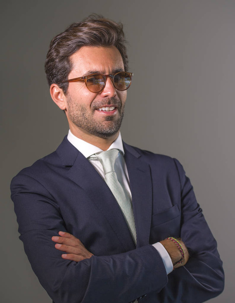 young elegant and handsome happy man in suit posing for company corporate business portrait relaxed and confident smiling happy isolated on grey as ceo executive businessman in sunglasses - Zdjęcie, obraz