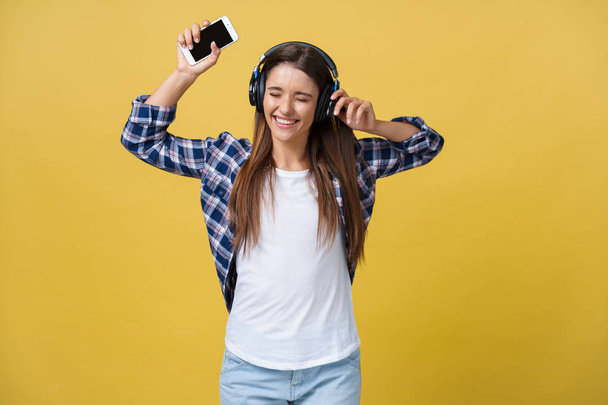 Lifestyle Concept - Portrait d'une belle femme caucasienne qui écoute joyeusement de la musique sur son téléphone portable. Fond jaune pastel studio. Espace de copie
. - Photo, image