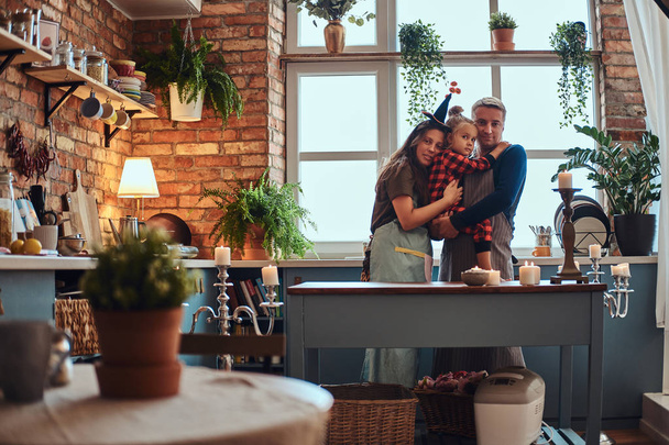Mom dad and little daughter embracing together in loft style kitchen at morning. - Photo, Image