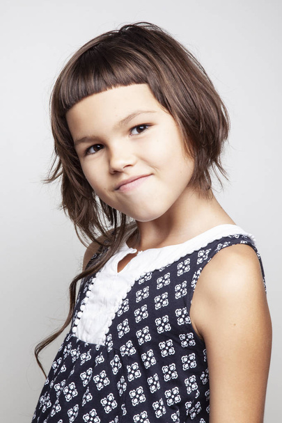 портрет милой маленькой девочки со стильной прической, смотрящей на камеру на белом фоне, крупным планом
 - Фото, изображение