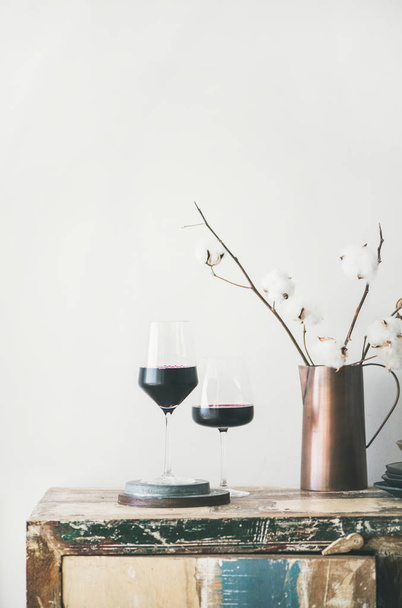 Two glasses of red wine and flowers over rustic kitchen countertop, white background behind - Foto, Imagen
