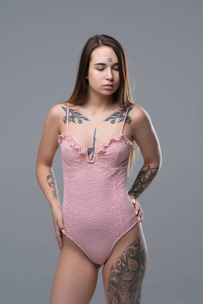 jovem menina bonita com tatuagem posando em estúdio em bodysuit rosa
 - Foto, Imagem