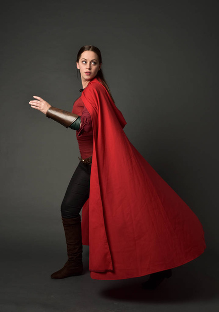 full length portrait of brunette girl wearing red medieval costume and cloak. standing pose   on grey studio background. - Foto, Imagem