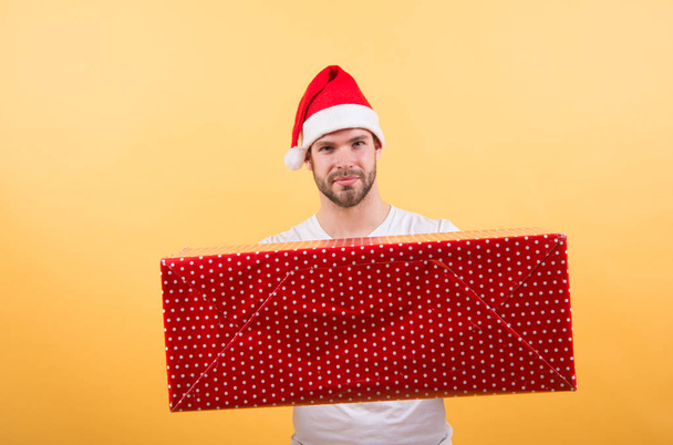 Man handsome unshaven santa hat hold gift box. Christmas gift concept. Santa bring gift for you. Man attractive santa claus carry big box. You deserve good gift. Christmas holiday celebration - Foto, afbeelding