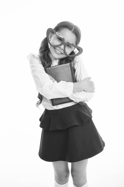 Girl cute big heart shaped glasses isolated white background. Child girl school uniform clothes holds book. Child wear school uniform smart kid smiling face. Back to school concept. Cute and smart - Zdjęcie, obraz