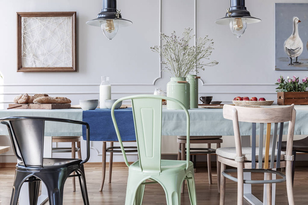 Colorful chairs at table in cottage grey dining room interior with lamps and posters. Real photo - Foto, Bild