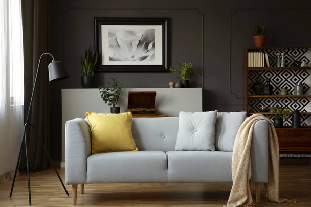 Comfy sofa with grey and yellow pillows, lamp, painting and cupboard in a living room interior. Real photo - Photo, Image