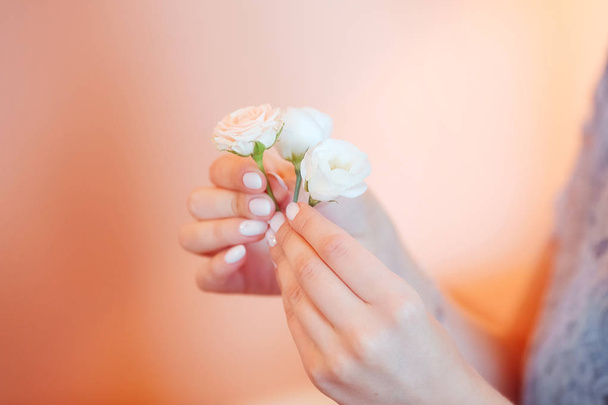 Delicate small roses in hands with a beautiful manicure on a pink background. Soft focus, background image - Foto, Bild