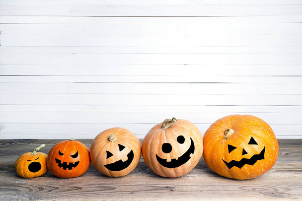 Halloween pumpkins with drawn faces on a wooden table on a background of white boards. Halloween background. Space for text. - Valokuva, kuva