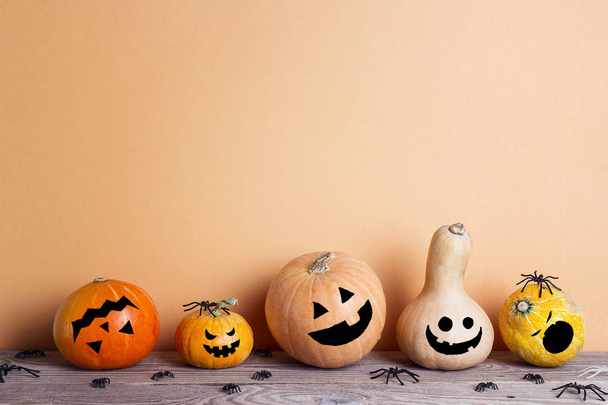 Halloween pumpkins with drawn funny faces on a wooden table on a orange background. Space for text. - Valokuva, kuva
