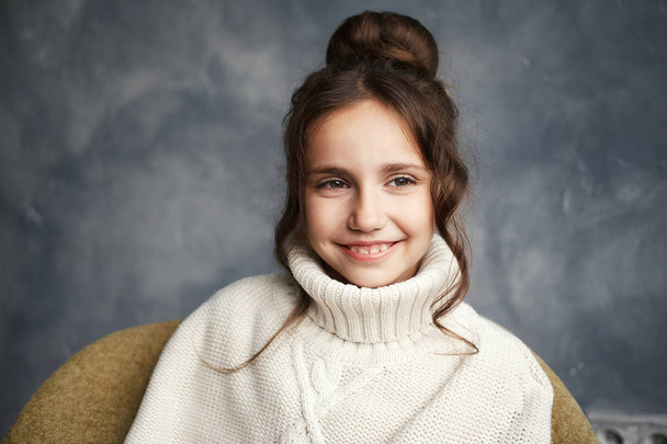 Portret van een lachende Kaukasische tienermeisje close-up. Curly brunette poseren binnenshuis. Trui kraag, koude, winter. - Foto, afbeelding