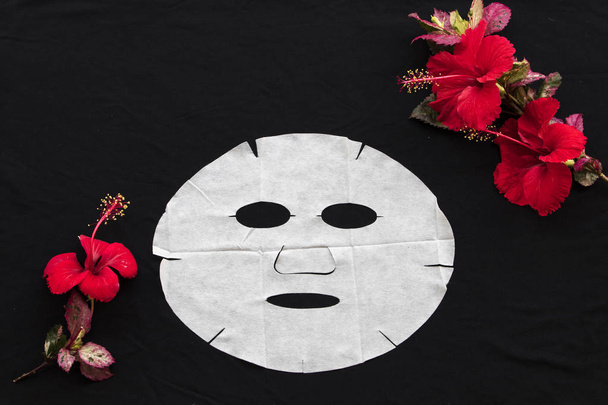 máscara de hoja de aroma natural para la cara de la piel de hierbas flores rojas hibisco esencia mascarilla en el fondo negro
  - Foto, imagen