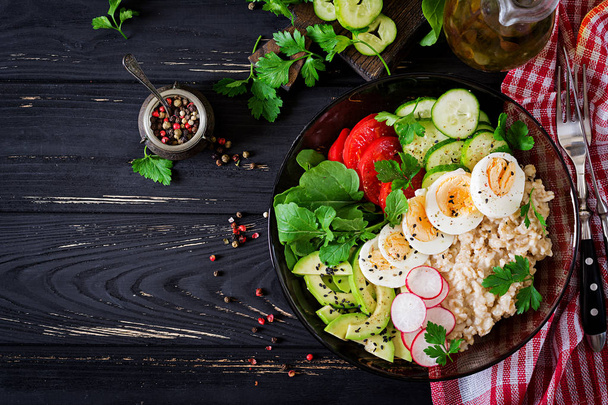 Healthy homemade salad of different fresh vegetables - tomatoes, avocado, cucumber, radish, egg, arugula and oatmeal in bowl. Diet food. - Photo, Image