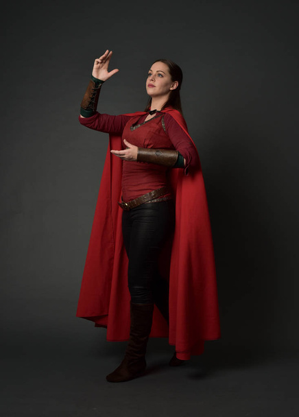 retrato de cuerpo entero de chica morena vestida con traje medieval rojo y capa. pose de pie sobre fondo gris estudio
. - Foto, imagen