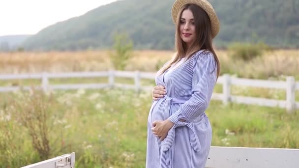 Zwangere vrouw in blauwe jurk en gebreide muts poses aan camera - Video