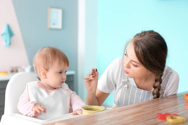 Young nanny feeding cute little girl, indoors - Photo, Image