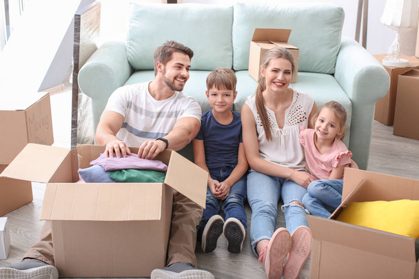 Young couple packing boxes with their children indoors. Happy family on moving day - Foto, Bild