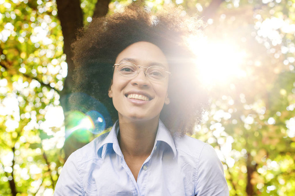Hermosa mujer negra feliz joven con gafas en la naturaleza, pelo rizado, sonrisa hermosa, estilo de vida sin preocupaciones, mirando a la cámara
 - Foto, Imagen