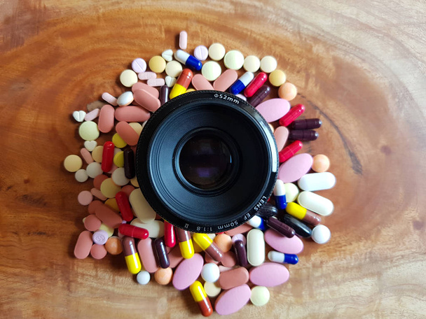 pila de pastillas para medicamentos tabletas cápsulas alrededor de la lente en fondo de madera
 - Foto, Imagen