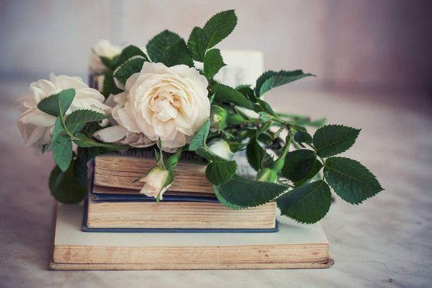white roses with leaves on stacked old books - 写真・画像