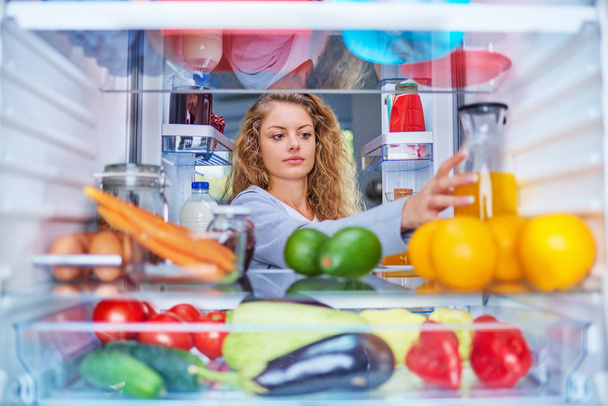 Frau nimmt Saft aus Kühlschrank voller Glukose. Frühstück zubereiten. Bild von innen aus dem Kühlschrank. - Foto, Bild