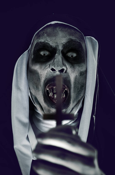 Closeup děsivé zlo jeptiška nosí typické černé a bílé zvyk, s vzhůru dolů kříž v ruce - Fotografie, Obrázek