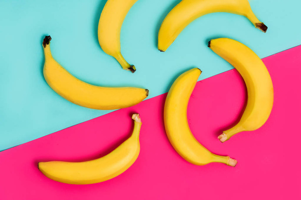 ピンクとパステル ブルーの背景に新鮮な黄色バナナのカラフルなフルーツ模様。上から見るから - 写真・画像