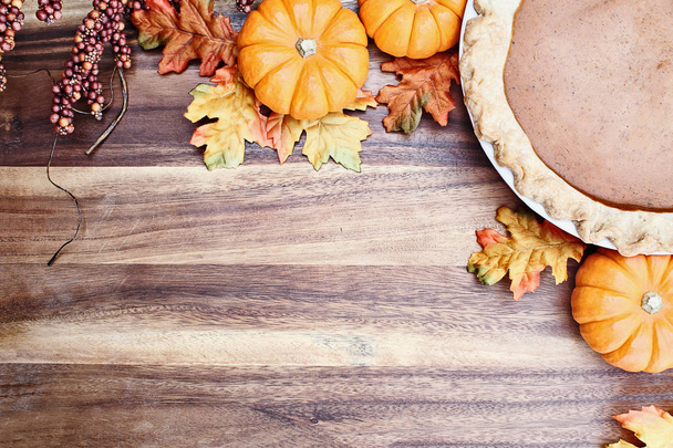 Homemade pumpkin pie in pie plate with little pumpkins, autumn leaves and room for text over rustic wooden background. Image shot from overhead. - Foto, immagini