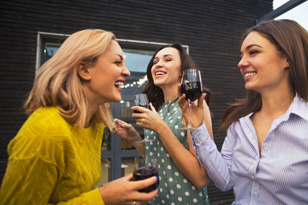 Kolme nuorta onnellista naista nauramassa, juomassa punaviiniä, pitämässä hauskaa. Puolue ja ystävyys käsite
.  - Valokuva, kuva