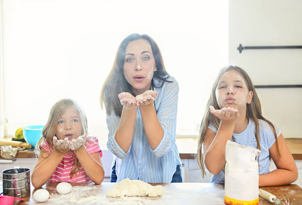Feliz joven madre y daughtesr verter harina a través de tamiz para la masa en la cocina divirtiéndose
 - Foto, Imagen