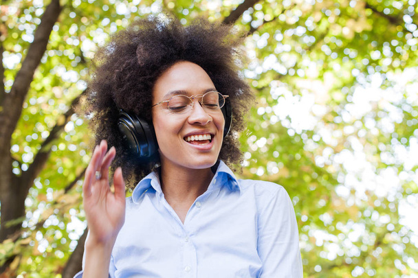 Retrato de una hermosa joven afroamericana feliz escuchando música en la naturaleza
 - Foto, Imagen