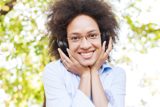 Portret van mooie gelukkig Afro Amerikaanse jonge vrouw luisteren muziek In de natuur - Foto, afbeelding