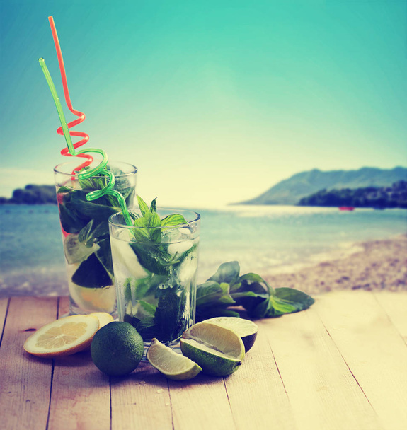 mojito cocktails with straws on wooden table with beach on background - Foto, immagini