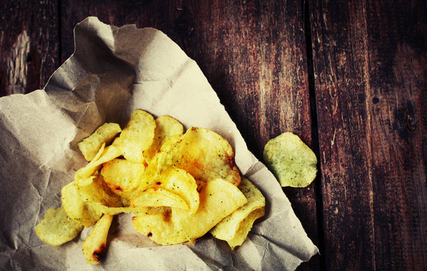 golden potato chips on paper on wooden table - Foto, Imagen