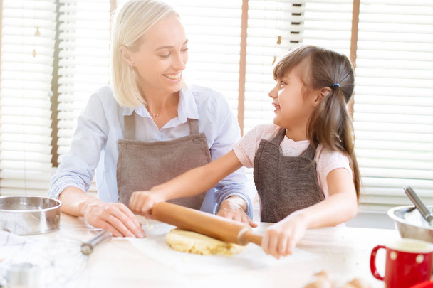 Cute girl and her mother bake kneading dough in the kitchen at home.Happy family and people concept.Mother's day. - Photo, Image