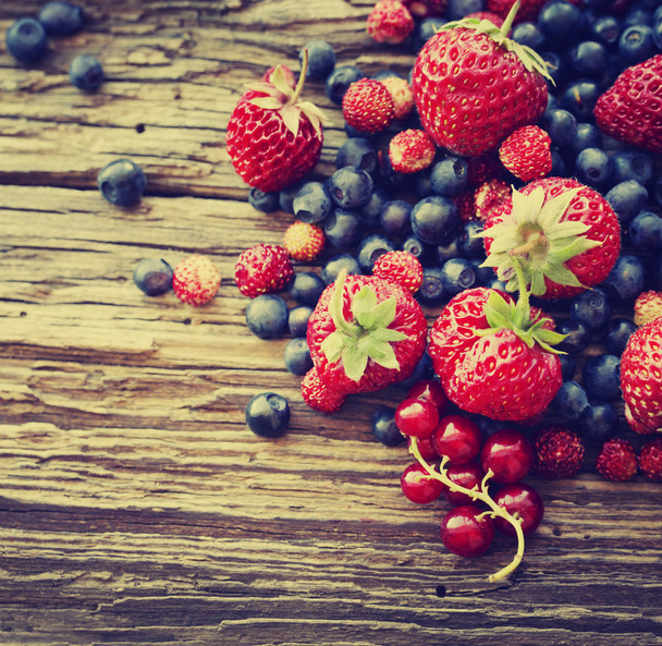 heap of fresh ripe blueberries and strawberries on wooden surface - Photo, Image