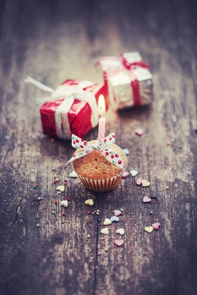 closeup view of cupcake with candle and colorful christmas decorations in vintage style over wooden background - Photo, image