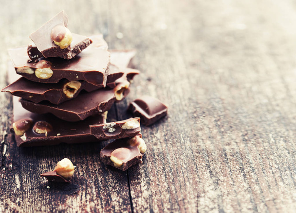 Broken chocolate with nuts on wooden background - Photo, image